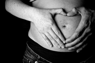 Midsection of woman with hand touching hair over black background