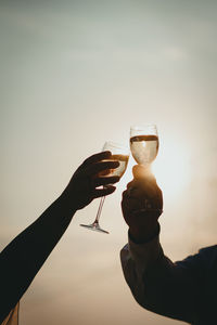 Close-up of hand holding wine glass against sky during sunset