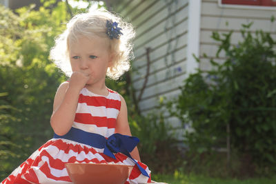 Pretty curly little girl seating in garden and eating berries from the plate.