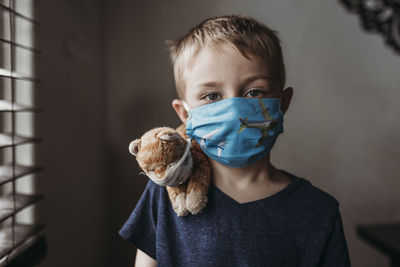 Close up of young school aged boy with mask on with stuffed animal negative space