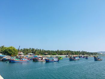 Boats moored in sea against clear blue sky