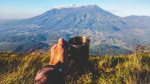 Cropped hand of man holding coffee in mug against mountains