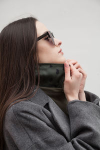 Close up side view postttait of young woman in grey coat standing against wall outdoors, outwear 