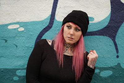 Young woman with pink hair standing against graffiti wall