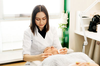 A cosmetologist performs a skin cleansing procedure in a cosmetology room, wipes his face