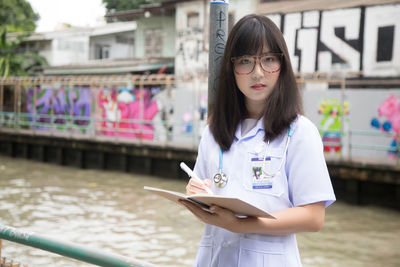 Portrait of female doctor holding book while standing outdoors