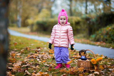 Portrait of cute girl standing by wicker basket with stuffed toy at roadside