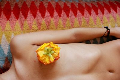 Midsection of woman with flower on breast lying on rug