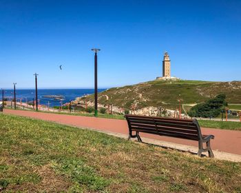 Empty bench by sea against clear blue sky