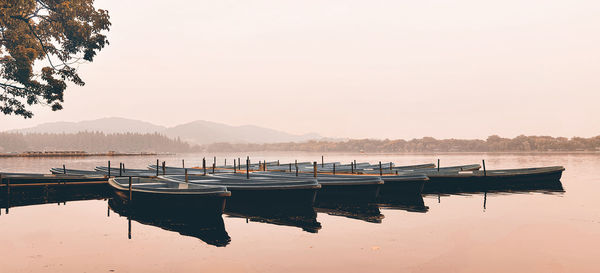 Boats moored in lake against sky during sunset