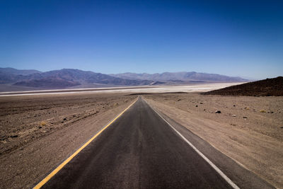 Empty road leading towards mountains against blue sky