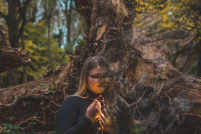 Young woman with illuminated lights standing by trees in forest