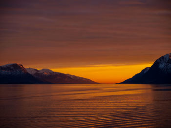 Scenic view of lake against dramatic sky during sunset