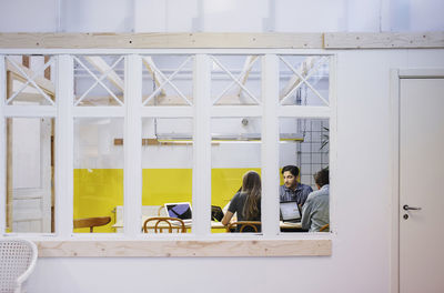 Four people discussing in meeting seen through glass window at office