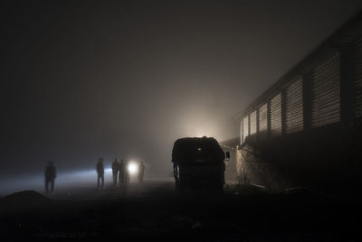 People walking by building against sky during foggy weather at night