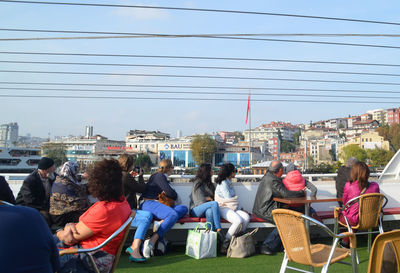 People sitting on seat in city against sky