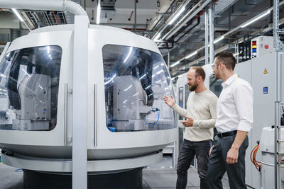 Employee and businessman talking at modern machine in a factory