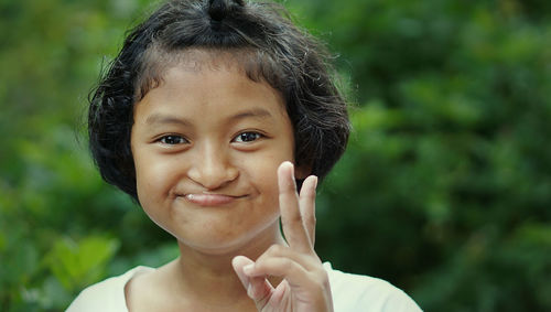Portrait of smiling girl gesturing peace sign outdoors