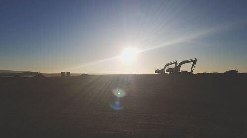 Silhouette construction vehicle on land against clear sky during sunset