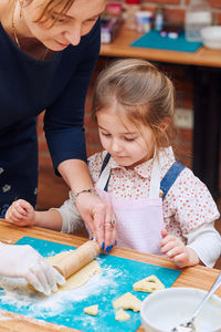 Girl looking at woman rolling dough