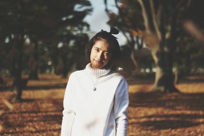 Portrait of young woman standing on field at park