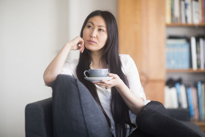 Young woman at home in a living room drinking tea and dreaming