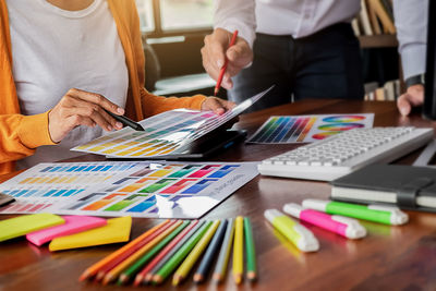 Midsection of creative occupation people pointing at color swatch sitting on table