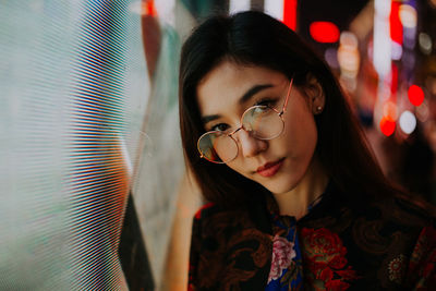 Portrait of young woman standing against illuminated city at night