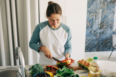 A woman in home clothes prepares a healthy vegetarian lunch, cuts vegetables for a salad.