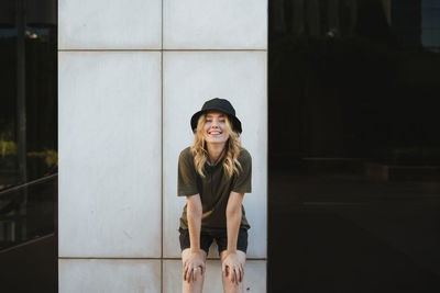 Portrait of smiling young woman standing against wall