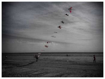 People flying over beach against sky