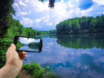 Midsection of man photographing by lake against sky