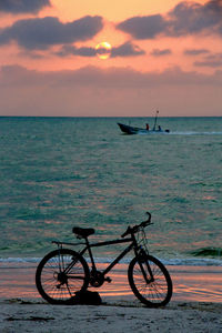 Bicycles on beach against sky during sunset