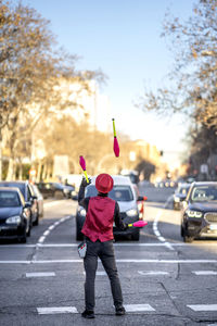 Solo performer juggling pins in front of cars on street