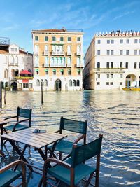 Chairs and table by river against buildings in city