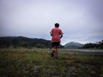 Rear view of man walking on field against sky