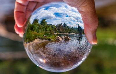 Close-up of person holding crystal glass against river 