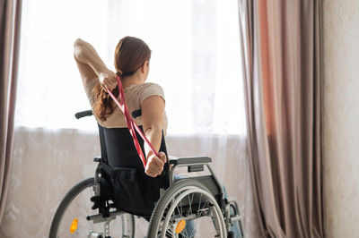 Rear view of woman exercising while sitting on wheelchair