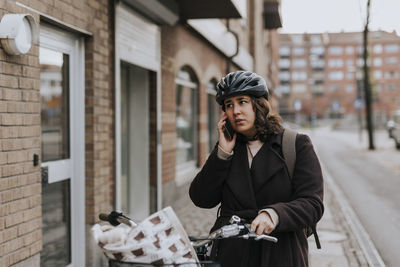 Young female commuter talking on smart phone with bicycle at footpath