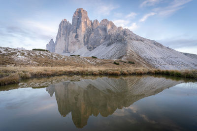 Sun setting over massive rock formation of tre cime reflecting in small pond, dolomites, italy