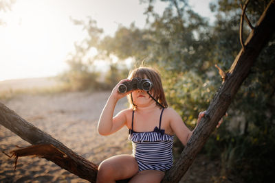 Cute european child girl in bathing suit with binoculars on tree. summer holidays and adventures.