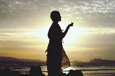 Silhouette man standing on beach against sky during sunset