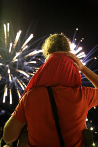 Rear view of man carrying daughter on shoulder while looking at firework display