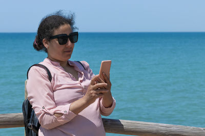 Portrait of young woman using mobile phone against sea