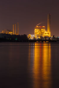 Illuminated buildings by river against sky at night