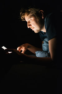 Side view of young man using mobile phone in darkroom