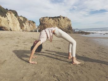 Woman practicing yoga at beach against sky