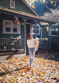 Full length of woman standing by building during autumn