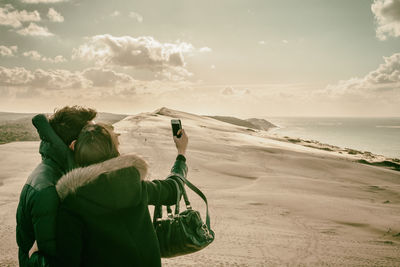 Couple taking selfie on sandy beach against sky