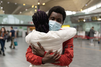 African couple wear face masks hugging each other within the new normality at airport terminal